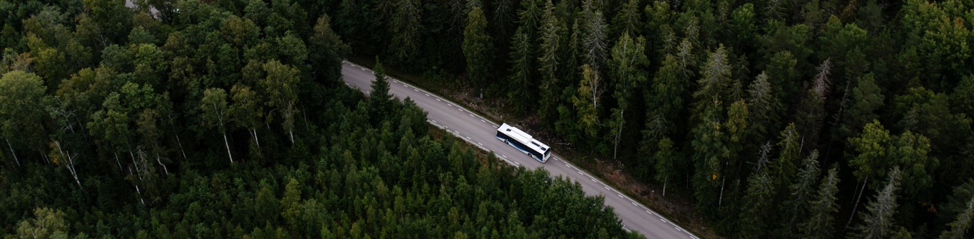 Drönarfoto som visar buss som kör på en väg i skogen.