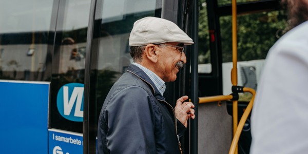 Äldre man som ler och är på väg att kliva ombord på en buss
