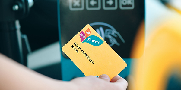 Hand som blippar gult skolkort mot biljettläsaren i bussen.