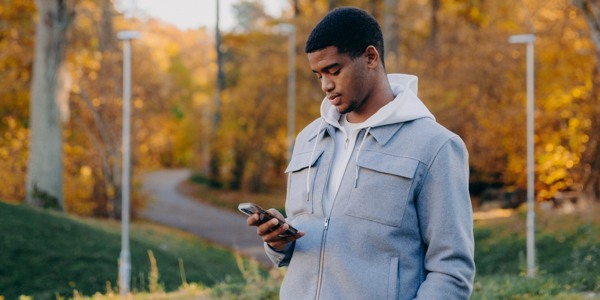 Ung man som står utomhus och tittar på sin mobiltelefon