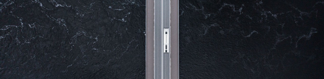 Drönarfoto som visar buss som kör på en bro över stormigt vatten.